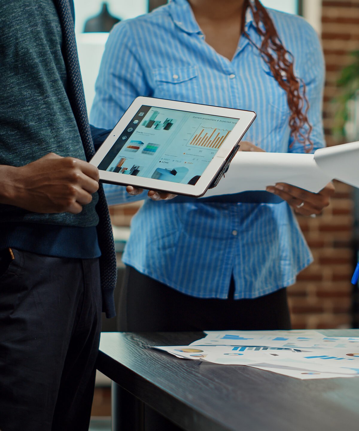 Colleagues using tablet and papers to analyze briefing results in boardroom meeting, working with statistics to build new business vision. Planning development strategy to increase profit.
